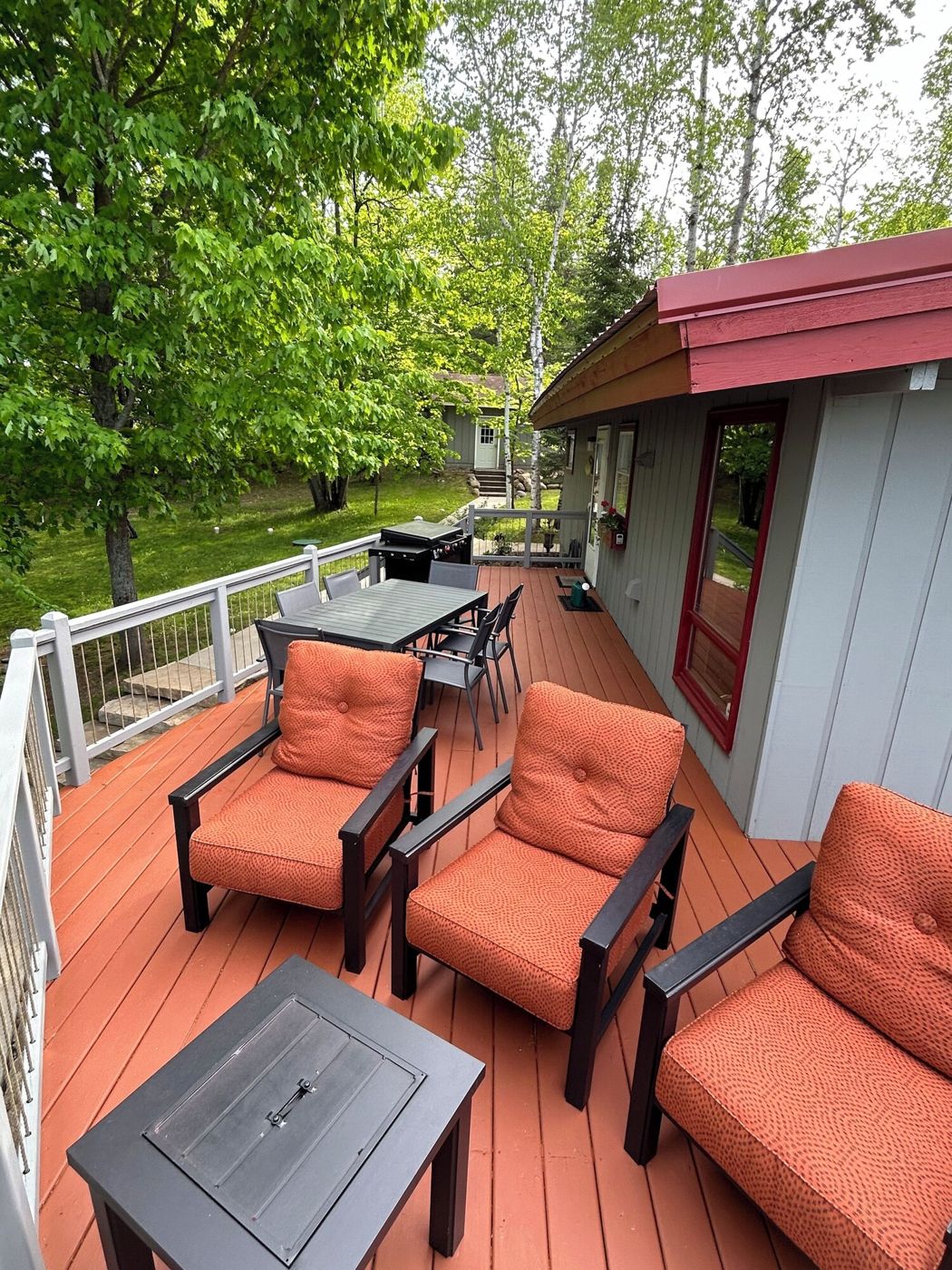 Wrap-around deck with orange cushioned chairs and a dining table
