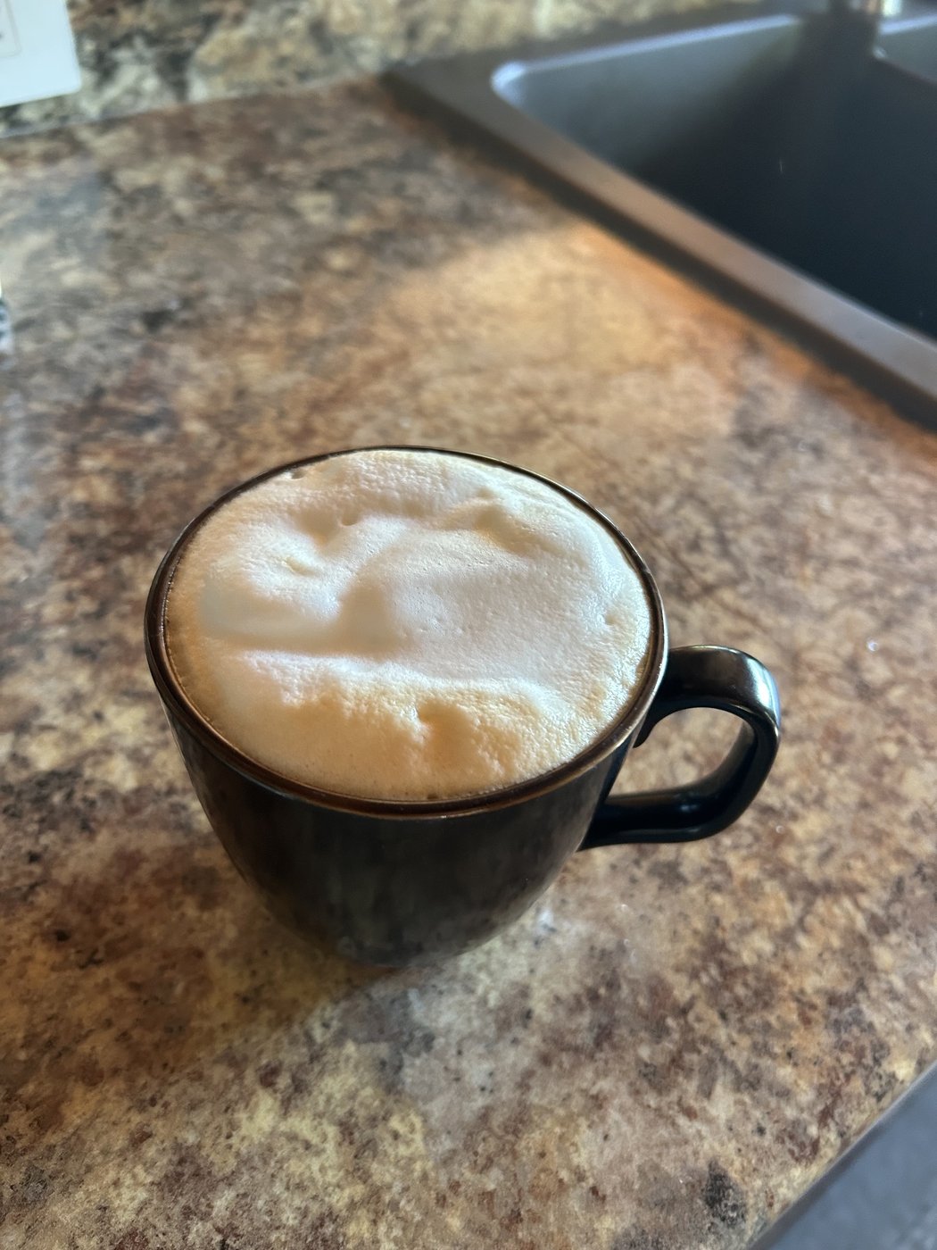 Frothy latte in a dark mug on the kitchen counter