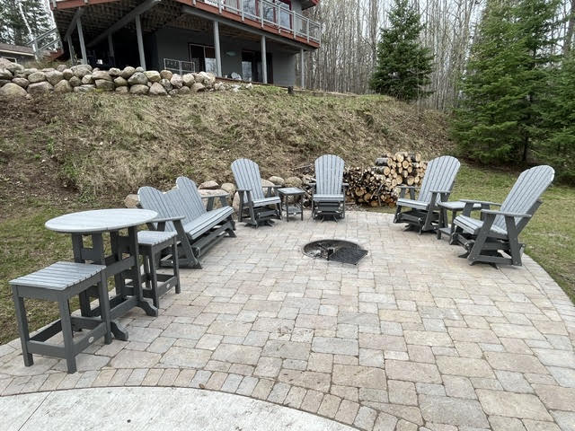 Lower stone patio with gray Adirondack gliders, a bench and a pub table around the fire pit